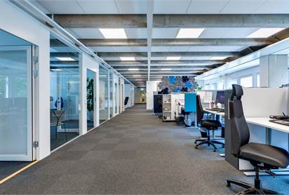 Kontorslandskap i korridor med glas och grått golv.