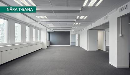Öppen kontorsyta med grå heltäckningsmatta och fönster längs ena väggen. Vretenvägen 9