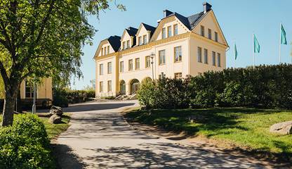 Fastigheten sedd från entrésidan med gångväg och grönska. Åldermansvägen 1
